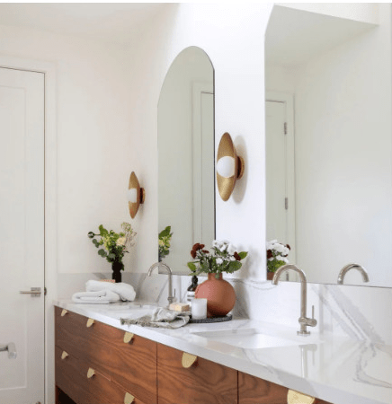 Modern bathroom featuring a double sink with elegant fixtures, a round mirror, and stylish decor, including potted plants and a neutral color scheme.