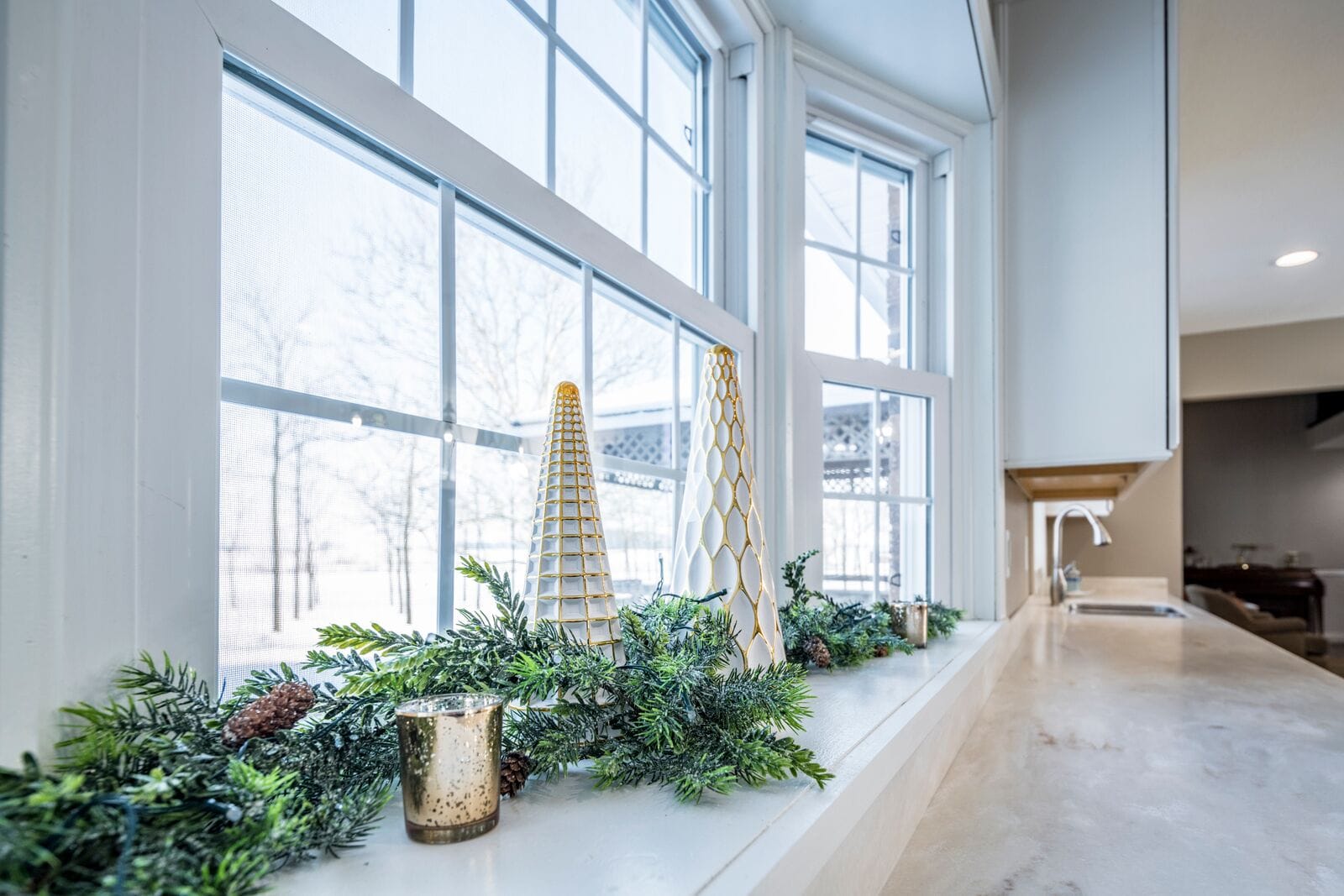 Winter decor featuring two white and gold cone-shaped figurines beside a greenery garland and a candle
