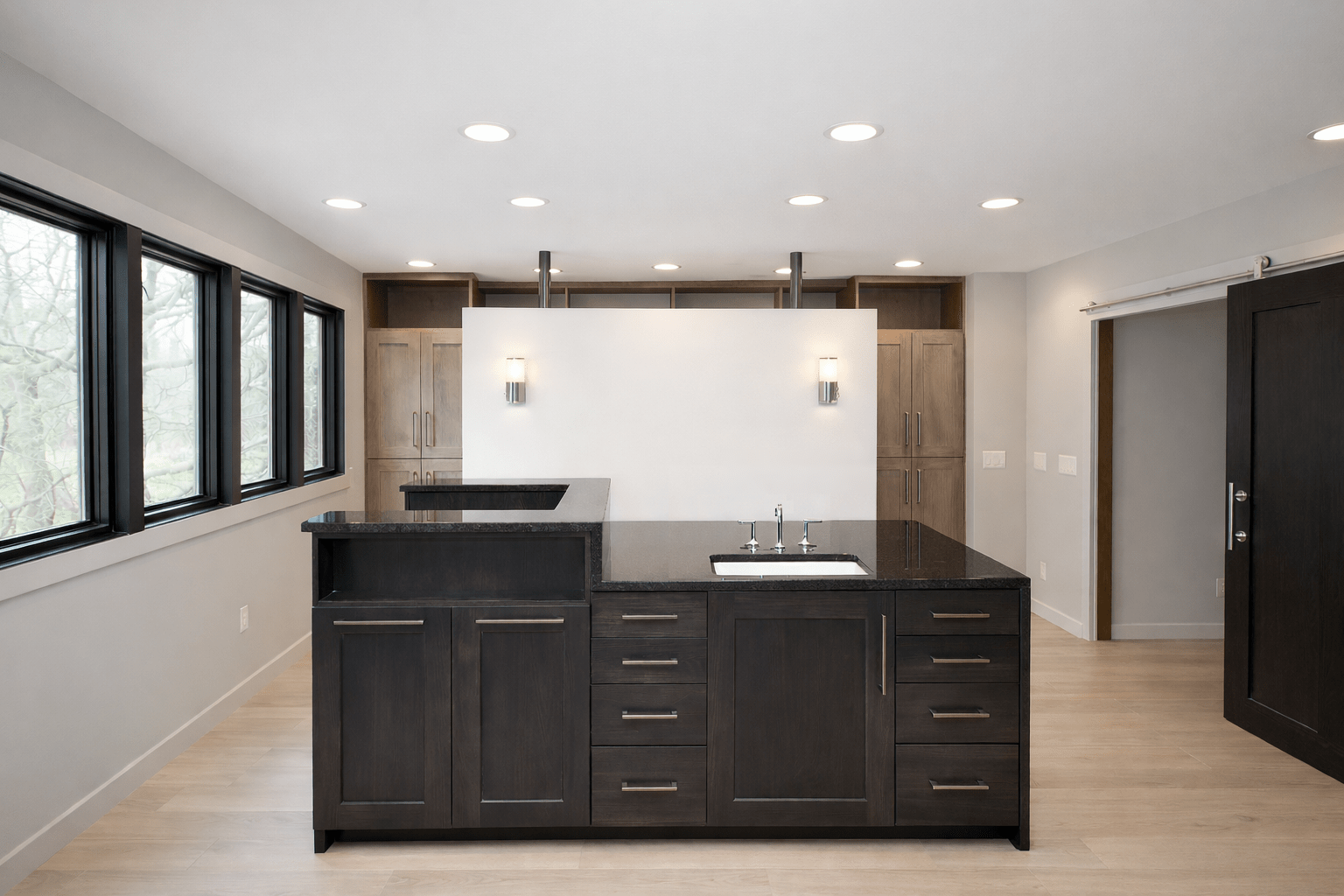 Modern kitchen featuring a dark wood island with a black countertop and sink, surrounded by large windows and light cabinetry, creating a bright space.
